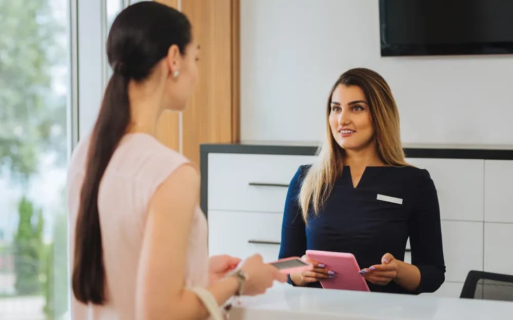 A receptionist welcoming a visitor at a clinic desk