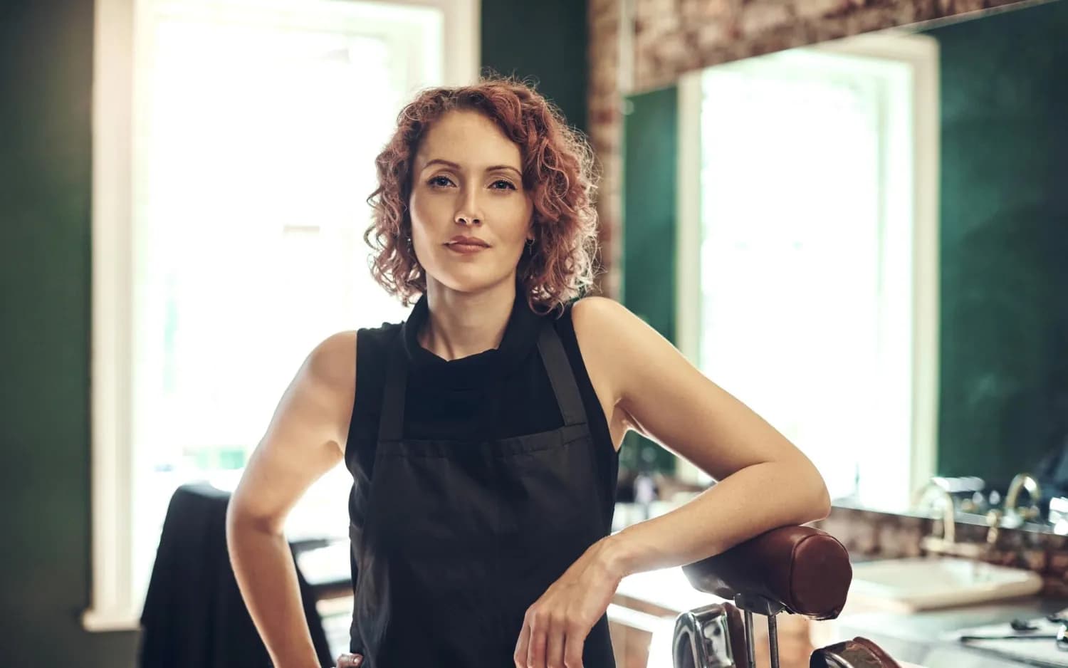 A salon owner leaning on a styling chair